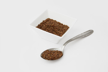 Flax seed in a ceramic container and in the metal spoon isolated on a white background