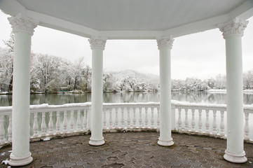 gazebo with roof and columns on a background of winter landscape with lake