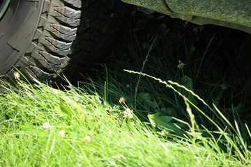 Fototapeta na wymiar Light and shadow - grass under the car covered by mud with detail of offroad tire, the foreground with bright light and background in dark of the car chassis