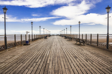 Wooden Skegness pier heading to the sea in the UK. Lamps, perspective, horizon and skies.