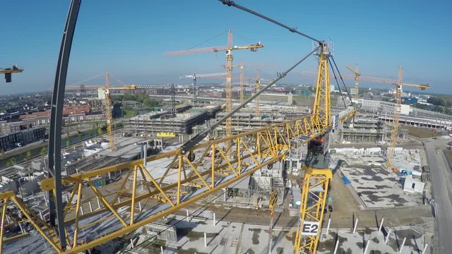 Aerial birds eye view of construction site drone moving close backwards past crane operating arm jib and showing more yellow tower cranes and underneath building site with concrete foundation 4k