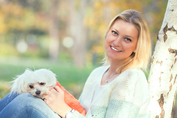 Portrait of beautiful young woman and her Maltese dog playing in a park on a nice autumn day
