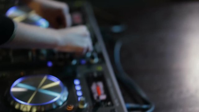 Woman DJ tweak different track controls on dj's deck at nightclub
