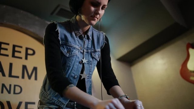 Woman DJ tweak different track controls on dj's deck at nightclub