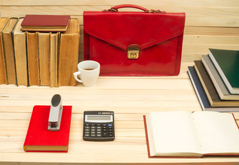 On a wooden table books, documents, calculator, red briefcase.