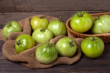 unripe green tomatoes on wooden table with sacking