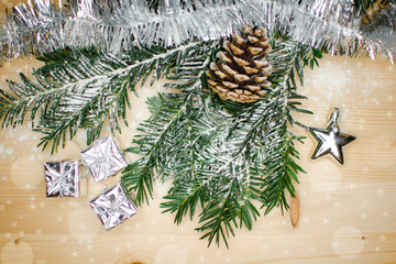 christmas branch winter decoration with stars, snow flakes ,snowman and little silver shiny presents and one big pinecone on wooden table