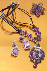 Silver fashion jewelry with purple rhinestones on orange mirror background 