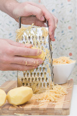 Man's hands with a grater grate the potatoes on the wooden board for potato pancakes in the kitchen. Healthy eating and lifestyle. © fotoduets