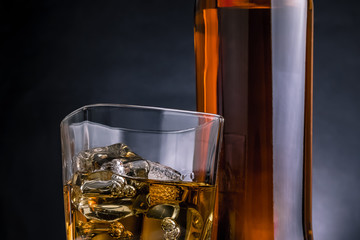 close-up of whiskey with ice cubes in glass near bottle on black background, cold atmosphere