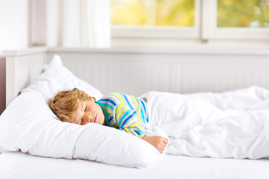 carefree little kid boy sleeping in bed in colorful nightwear.