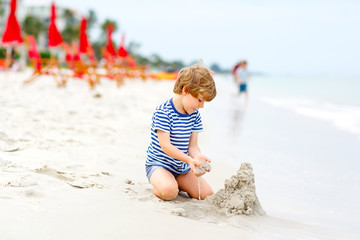 Little kid boy having fun with building sand castles
