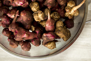 Fresh natural Jerusalem artichokes or sunchokes in a metal colander with a brown wood background