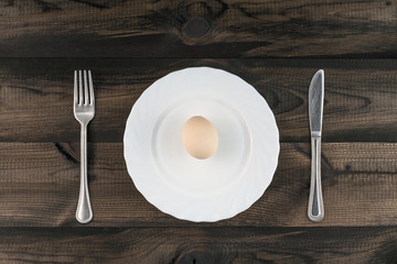egg on white plate with fork and butter knife on wooden table