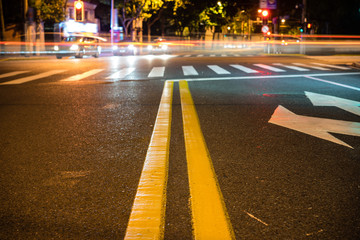 Nights lights of the big city, the night avenue with road markings and headlights of the approaching cars, close up view from asphalt level © Leo Li