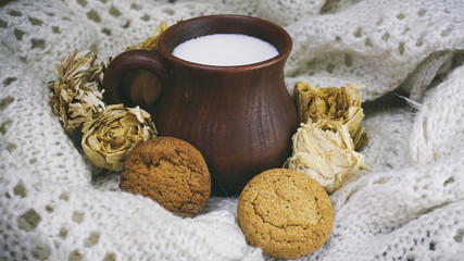 earthenware Cup with milk and cookies at the white knitted scarf