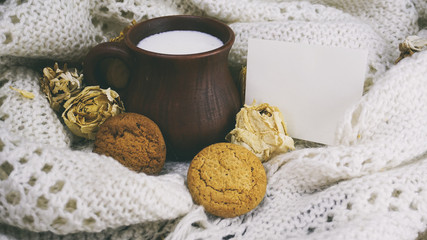 Obraz na płótnie Canvas earthenware Cup with milk and cookies at the white knitted scarf