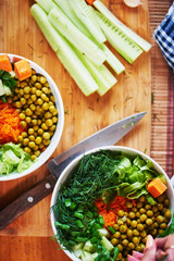 Top view of vegetable mix in bowls with green peas, cucumbers, carrots, lettuce and dill, standing on a wooden table