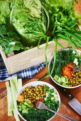 Vegetable mix in bowls with green peas, cucumbers, carrots, lettuce and dill, standing on a wooden table