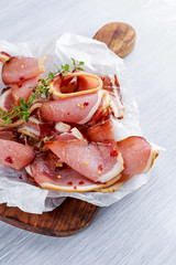 Raw beer bacon slices on crumpled paper which herbs