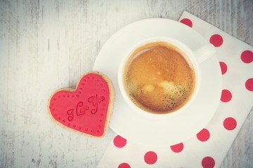 Valentines day background. Top view of a heart shaped cookie and a cup of coffee over a white wood rustic background. Vintage effect.