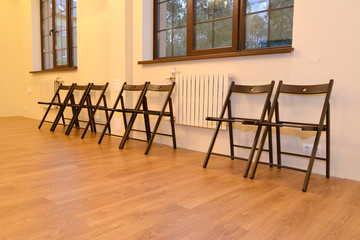 Wooden chairs stand in a row along a wall in the hall. Interior