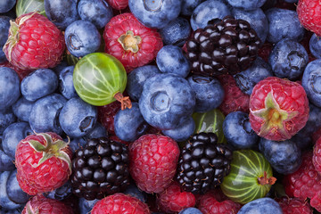 Blueberries, raspberries, blackberries and gooseberries background shot top down. Top view.