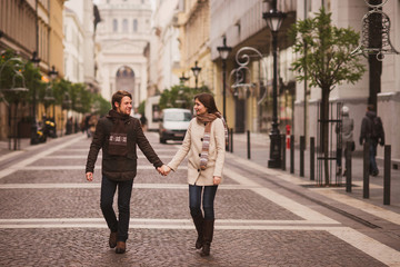 Fototapeta premium Boże Narodzenie na starym mieście. Młoda wesoła para kaukaski w ciepłym, przytulnym ubraniu spaceru w centrum miasta.