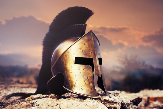 Spartan helmet on ruins with sunset sky.