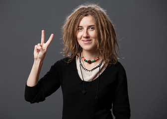 Beautiful hipster woman with dreadlocks showing peace gesture and smiling,  gray background