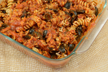 Casserole preparation of cooked whole wheat rotini pasta, ground turkey meat, sliced black olives and tomato sauce in glass baking dish