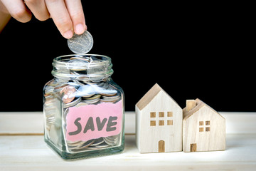 Hand putting coin in glass jar of coin for saving money for buying house