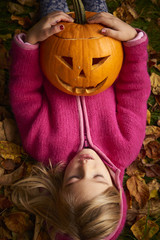Child cute blond girl playing in autumn leaves with halloween pumpkin.
