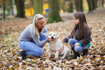 Mother and daughter with their labrador retriever puppy in park.