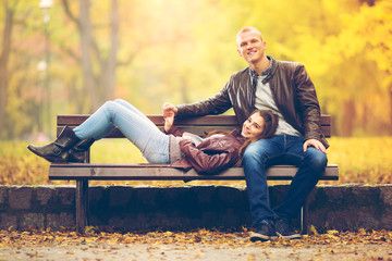 Young couple is on a bench in a park on a beautiful Autumn day.