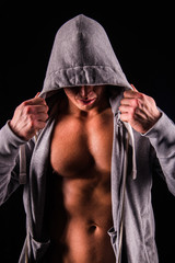 Obraz na płótnie Canvas Portrait of sexual strong young man with muscular body in grey sport jacket hooded on dark background