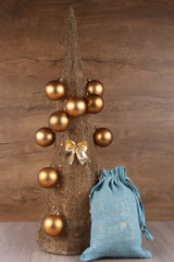 Decorative Christmas tree made from straw  with golden balls and blue jute Santa gifts bag on wooden background