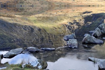 Brown, rocky mountainside reflected in lake.    Wales