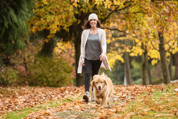 Happy woman walking her Golden Retriever Dog in a park with Fall