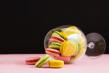 Multicolored macaroon in wine glass on a black and pink background. The author's processing, selective focus, film effect,