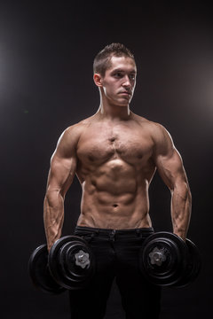 young man bodybuilder looking sideways holding dumbbells