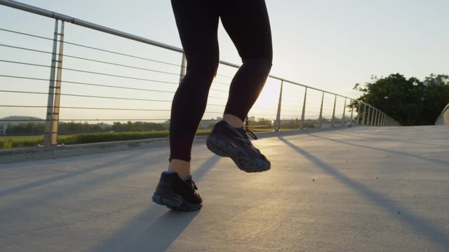 SLOW MOTION: Female runner running across city bridge into magical setting sun