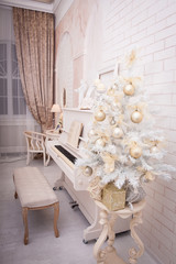 White piano near decorated Christmas tree in large hall with brick wall. Xmas background. Winter time