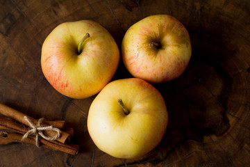 Three golden apples and cinnamon sticks on wooden background. Top view. Golden-yellow colors.