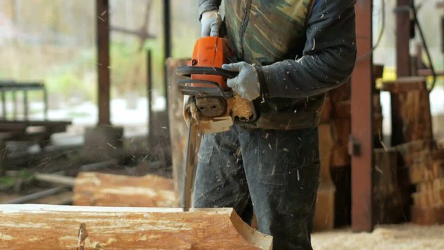 Man makes curly cutting wood Chainsaw. The log will be part of the future of the wooden house. Protective face mask on the face of the builder and a lot of sawdust.