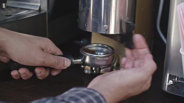 Tracking with close up of male barista hands putting grounds into filter of machine and making coffee