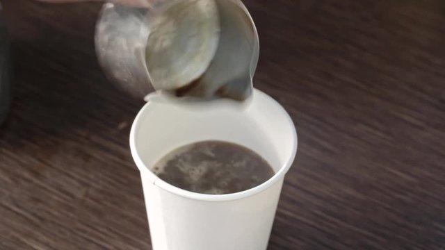 Hands of male barista pouring fresh coffee into biodegradable cup, putting milk into it and adding cinnamon 