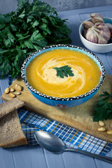 cream soup with pumpkin, greens, seeds and bread on a blue backg