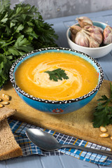 cream soup with pumpkin, greens, seeds and bread on a blue backg