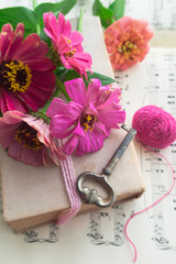 Old book with vintage key and pink flowers zinnia on music sheet background